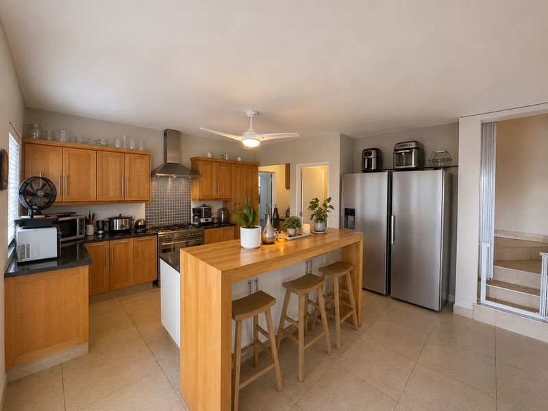 A well-maintained kitchen featuring wooden cabinetry, granite countertops, a gas hob with extractor fan, and a central breakfast bar island.