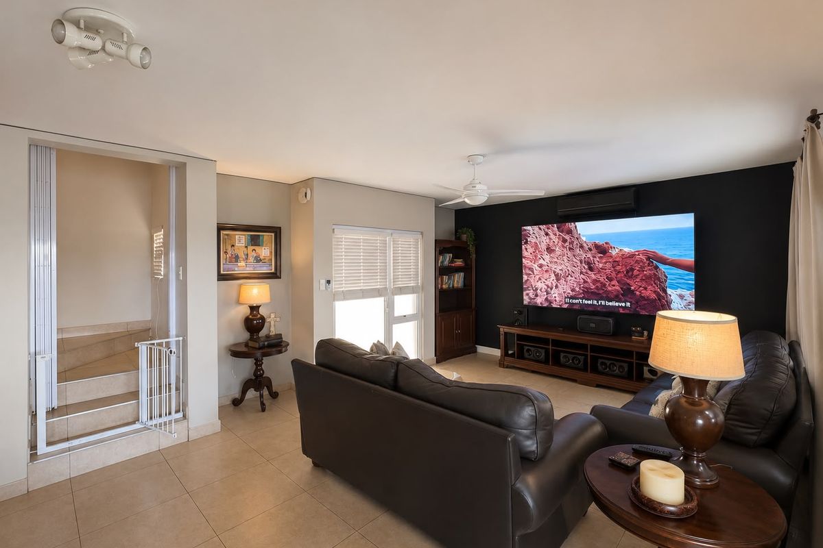 A comfortable living room featuring tiled flooring, a ceiling fan, split-system air conditioning, and a staircase leading to the upper level.
