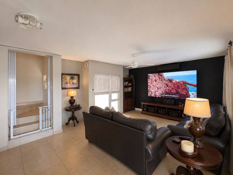 A comfortable living room featuring tiled flooring, a ceiling fan, split-system air conditioning, and a staircase leading to the upper level.