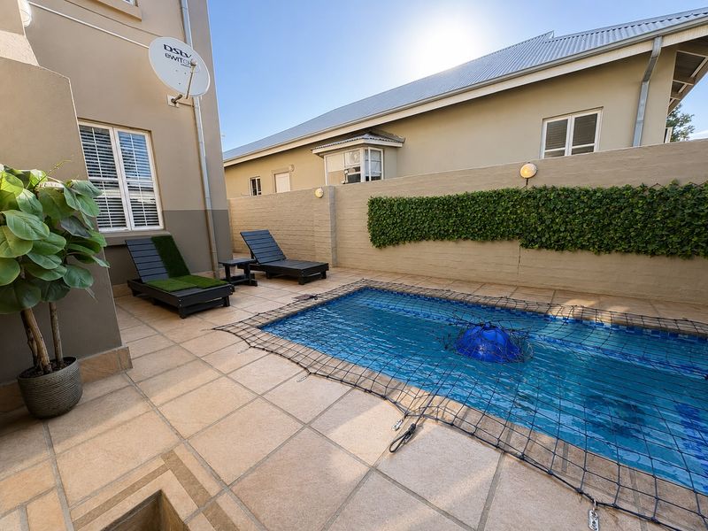 A private courtyard featuring a swimming pool with a safety net, surrounded by tiled patio space and a secure boundary wall.