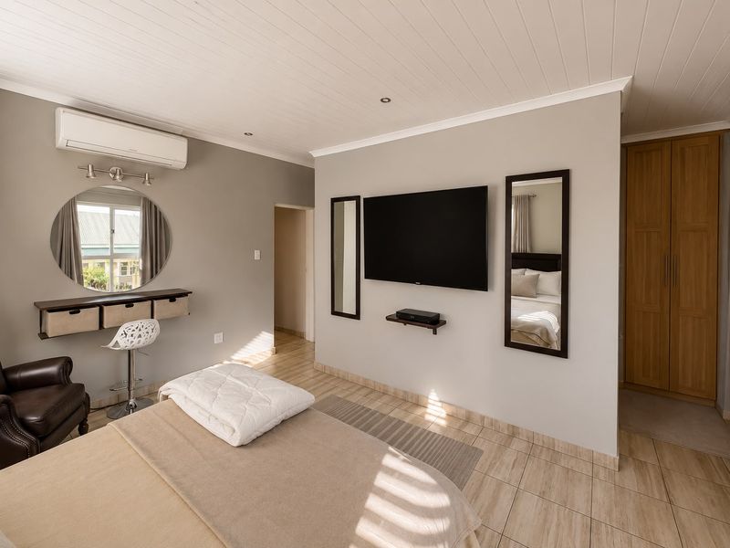 A well-maintained bedroom featuring tiled flooring, a tongue and groove ceiling, built-in wooden wardrobe, and a wall-mounted split-system air conditioner.