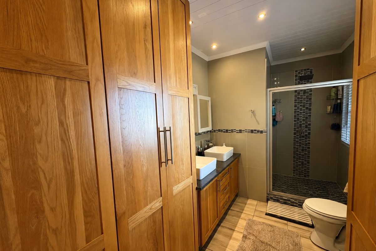 Modern bathroom featuring a double vanity with vessel sinks, extensive built-in wooden cabinetry, and a tiled walk-in shower with recessed lighting.