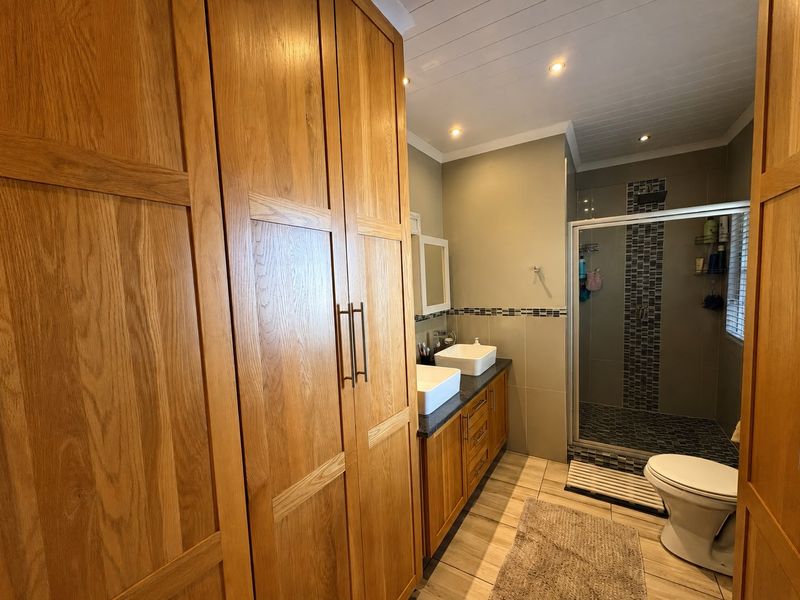 Modern bathroom featuring a double vanity with vessel sinks, extensive built-in wooden cabinetry, and a tiled walk-in shower with recessed lighting.