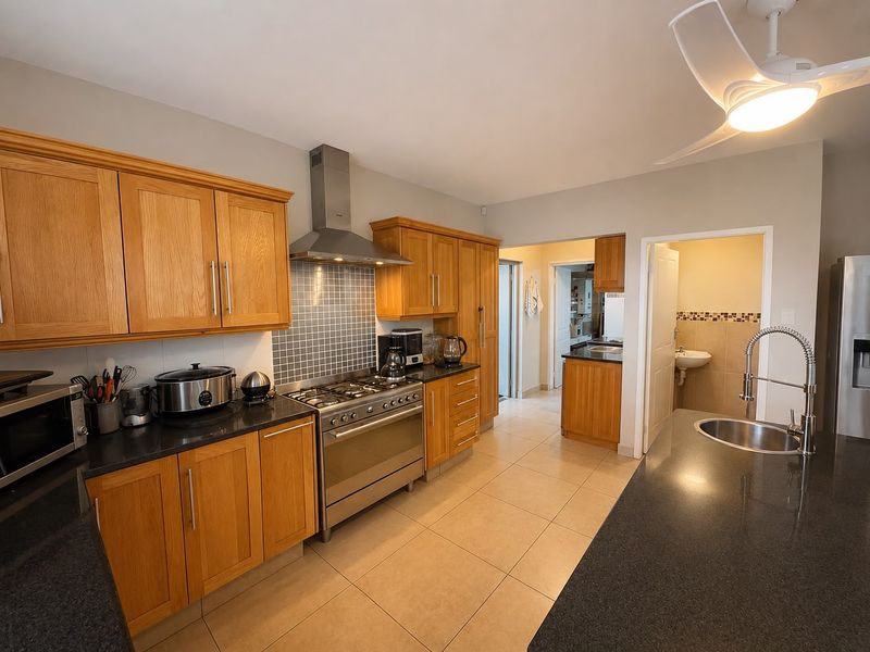 Spacious kitchen featuring wooden cabinetry, granite countertops, a gas stove with extractor fan, and a central island with a modern gooseneck faucet.