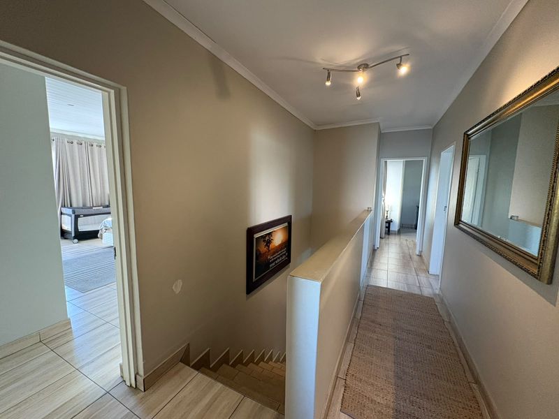 A bright upper-level hallway featuring tiled flooring, a staircase with a half-wall balustrade, and access to adjacent bedrooms.
