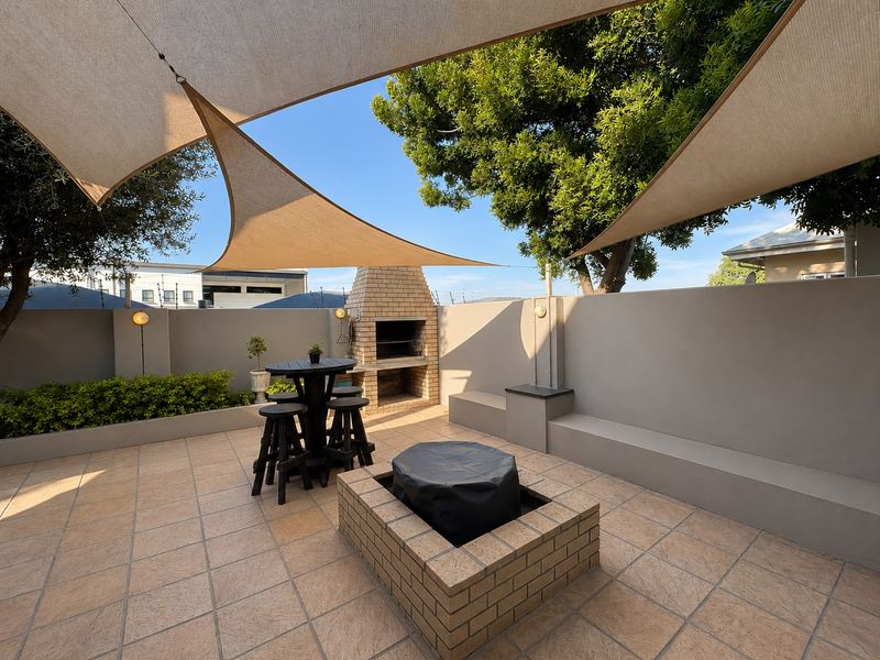 Outdoor patio area featuring a built-in brick braai, fire pit, integrated bench seating, and overhead shade sails, perfect for entertaining.