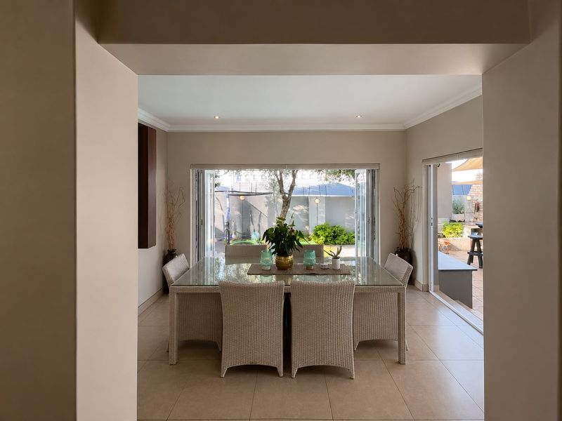 A bright dining area featuring large folding glass doors that open onto an outdoor patio, complemented by neutral tiled flooring and recessed ceiling lighting.