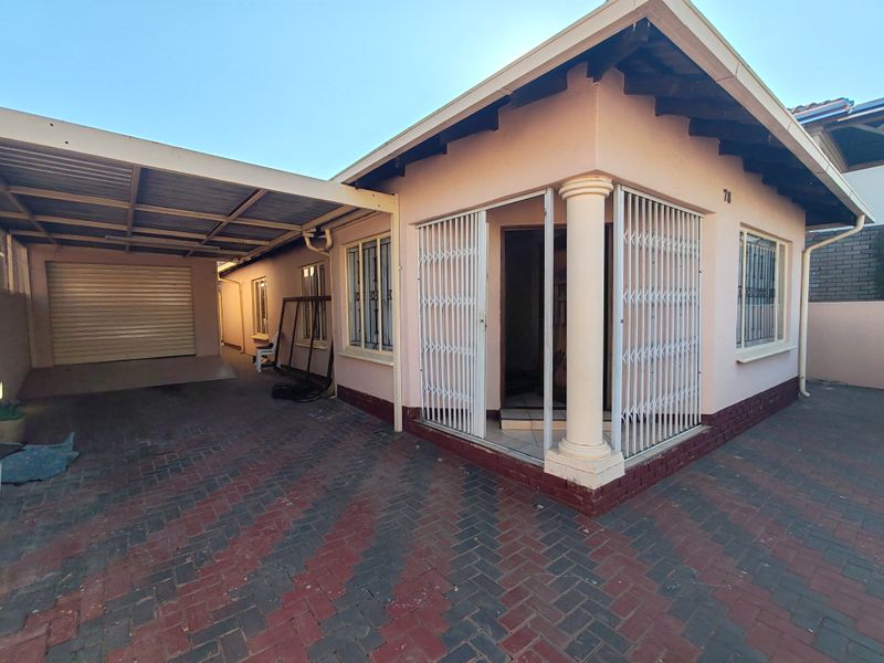 Front exterior view of the house featuring a paved driveway, attached carport, and a secure entrance with a decorative column.