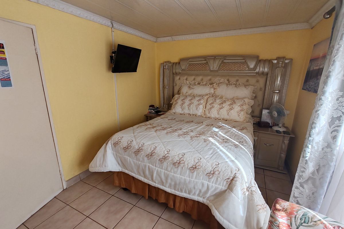 A bedroom featuring tiled flooring, decorative ceiling coving, and a ceiling rose. The space requires cosmetic updates to finishes and improved cable management.