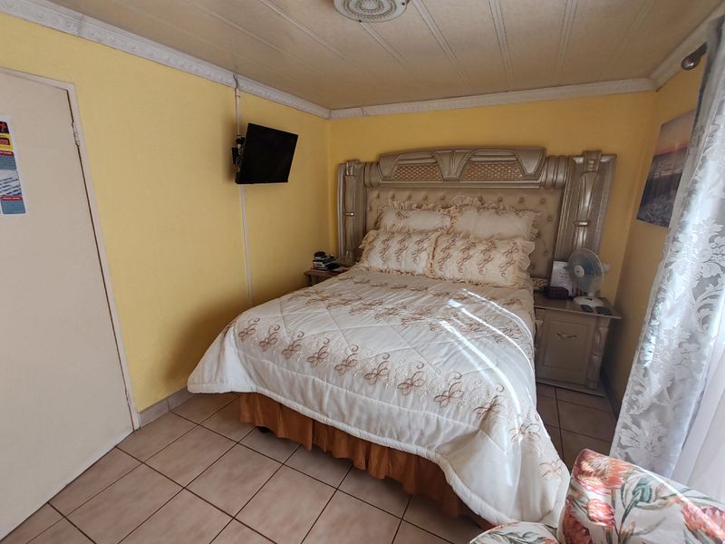 A bedroom featuring tiled flooring, decorative ceiling coving, and a ceiling rose. The space requires cosmetic updates to finishes and improved cable management.