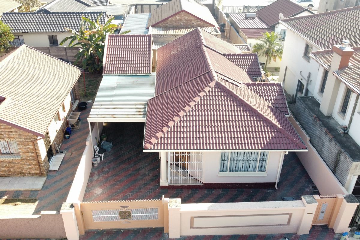 Aerial view of a residential property featuring a tiled roof, a covered carport, a paved driveway, and secure boundary walling.
