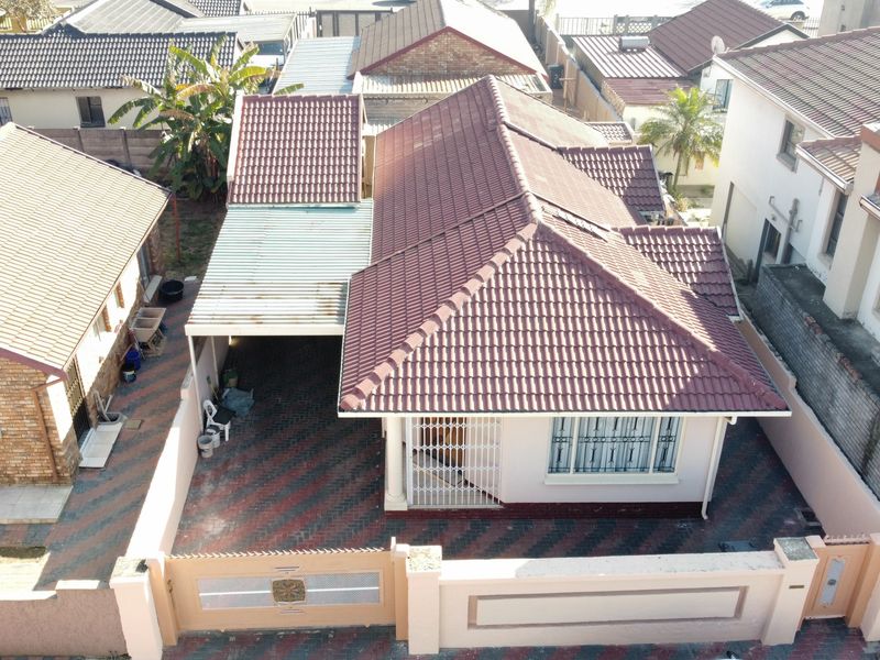 Aerial view of a residential property featuring a tiled roof, a covered carport, a paved driveway, and secure boundary walling.