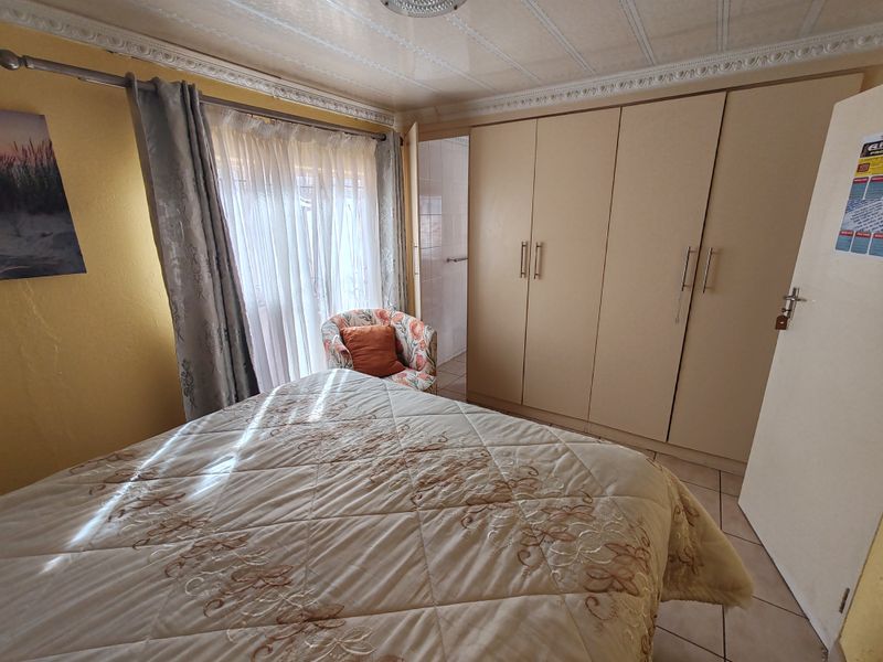 A bedroom featuring built-in cupboards, tiled flooring, and decorative ceiling cornices, offering a functional space with natural light.
