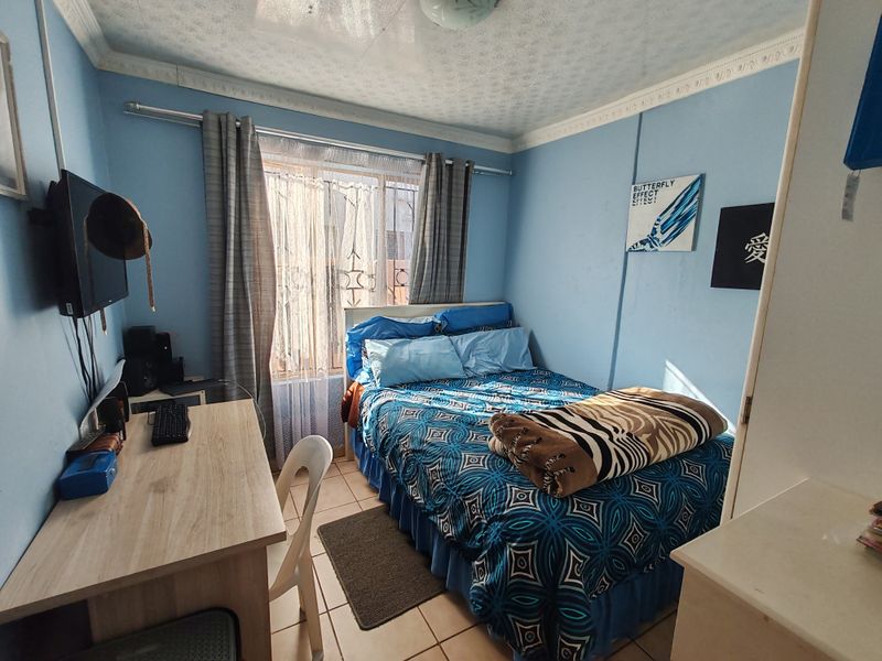 A compact bedroom featuring tiled flooring, decorative ceiling cornicing, and a window fitted with security bars.