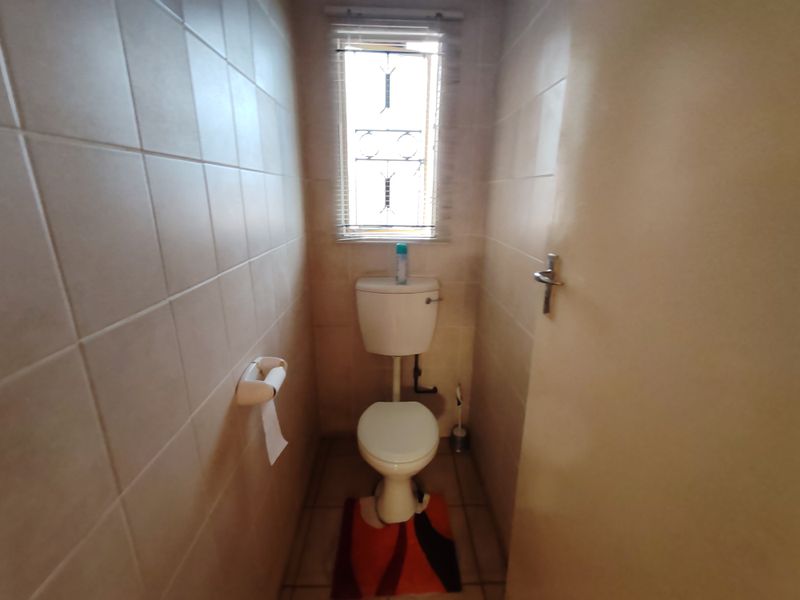 A compact, tiled guest toilet featuring a standard white toilet suite and a small window with security bars.