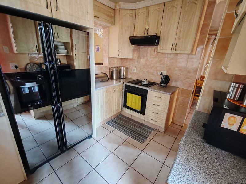 A functional kitchen featuring built-in cabinetry, tiled splashbacks, and integrated appliances, offering a practical layout with potential for modern cosmetic updates.