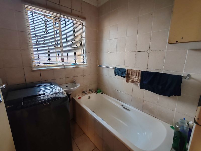 A functional bathroom featuring a bathtub, wall-mounted basin, and tiled finishes, requiring cosmetic updates to improve its overall condition and aesthetic appeal.