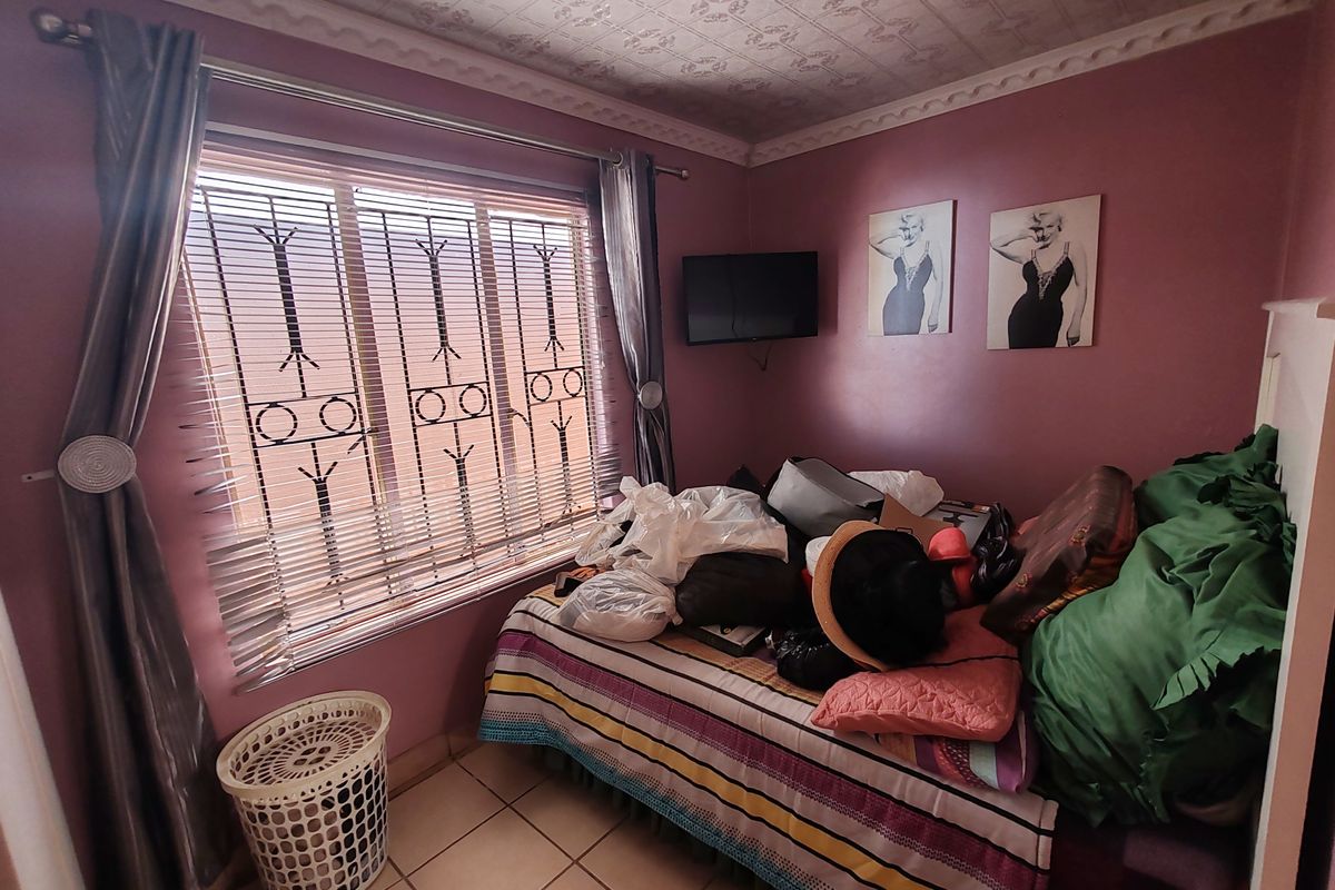 A bedroom featuring tiled flooring, decorative ceiling tiles, and security bars on the window. The space requires cosmetic updates to improve its overall appeal.