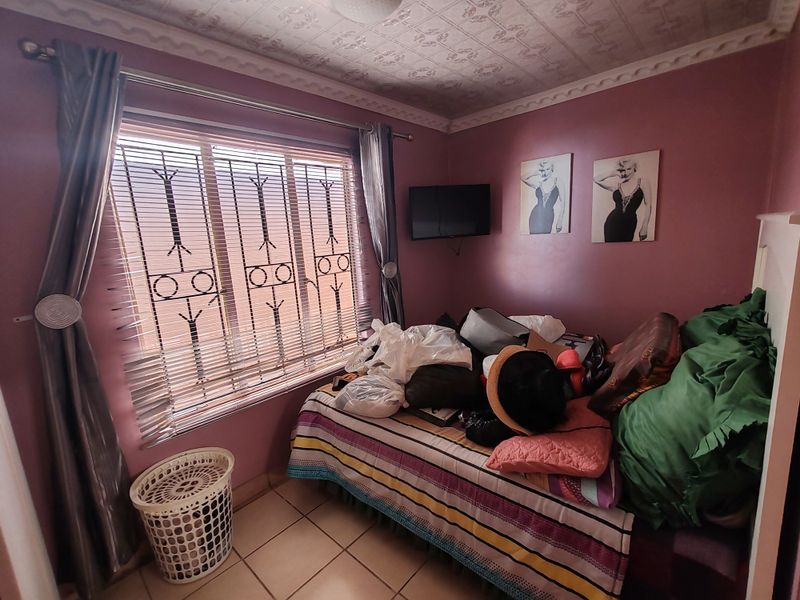A bedroom featuring tiled flooring, decorative ceiling tiles, and security bars on the window. The space requires cosmetic updates to improve its overall appeal.