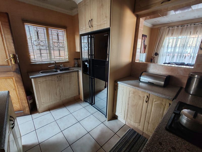 A functional kitchen featuring laminate cabinetry, granite countertops, a stainless steel sink, and a built-in gas hob with ceramic tiled flooring.