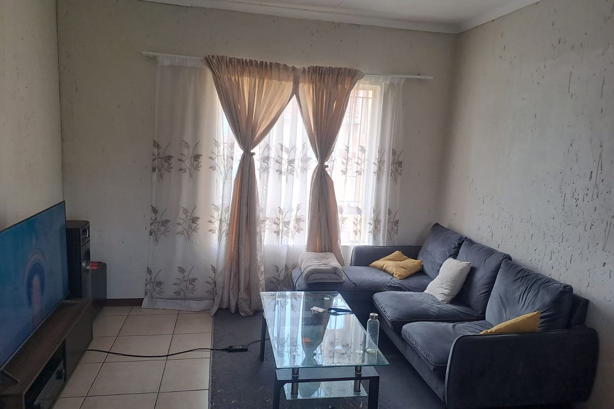 A living room featuring tiled flooring and a window with curtain fixtures, currently showing significant wear and damage to the wall surfaces.