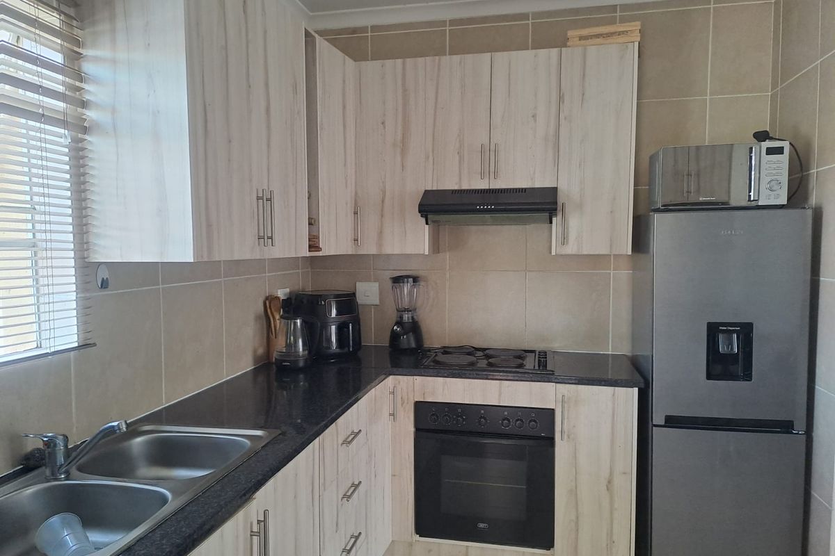 Functional kitchen featuring light wood-look cabinetry, granite countertops, a double stainless steel sink, and built-in oven with electric hob.