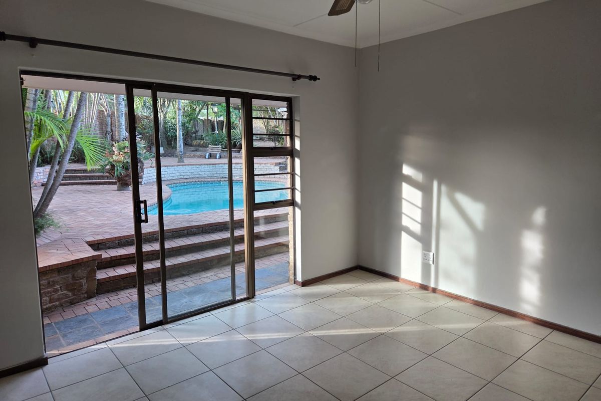 Bright, empty living room featuring tiled flooring, a ceiling fan, and large sliding glass doors providing direct access to the outdoor pool area.
