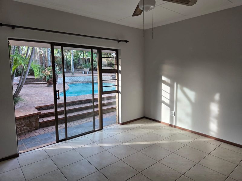 Bright, empty living room featuring tiled flooring, a ceiling fan, and large sliding glass doors providing direct access to the outdoor pool area.