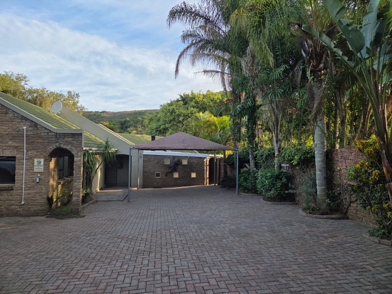 A spacious brick-paved driveway leading to the front entrance, featuring a carport and established garden surroundings.