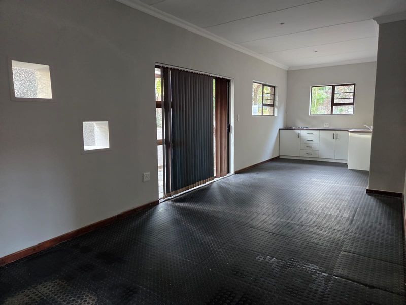 An open-plan living and kitchen area featuring neutral walls, durable rubber flooring, and direct access to the exterior through a sliding glass door.