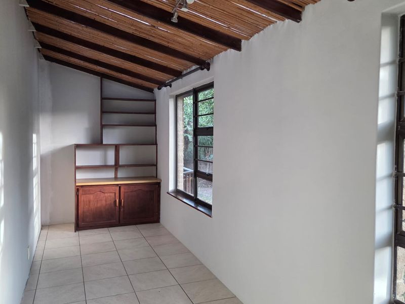 A covered patio area featuring a bamboo ceiling, tiled flooring, and built-in wooden shelving, offering a versatile space for outdoor living.