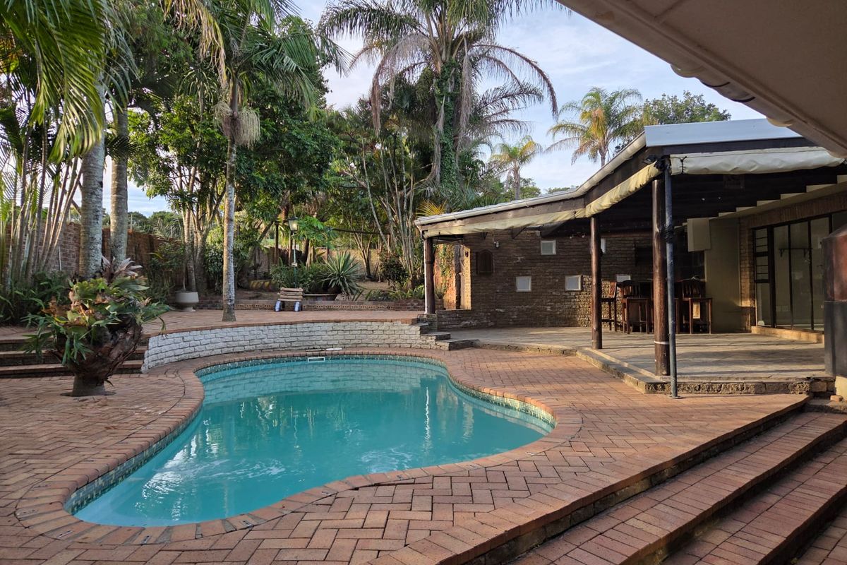 Outdoor entertainment area featuring a swimming pool, brick paved surround, and a covered patio space with timber support structures.