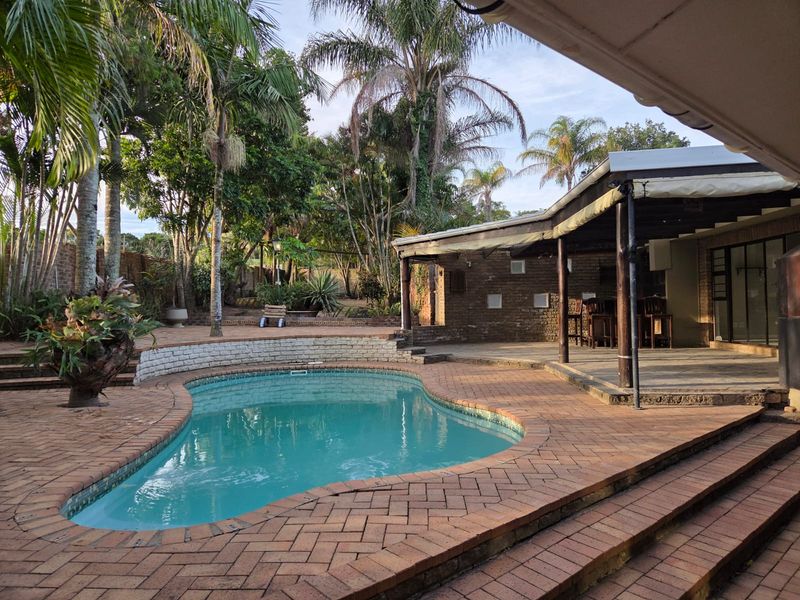 Outdoor entertainment area featuring a swimming pool, brick paved surround, and a covered patio space with timber support structures.