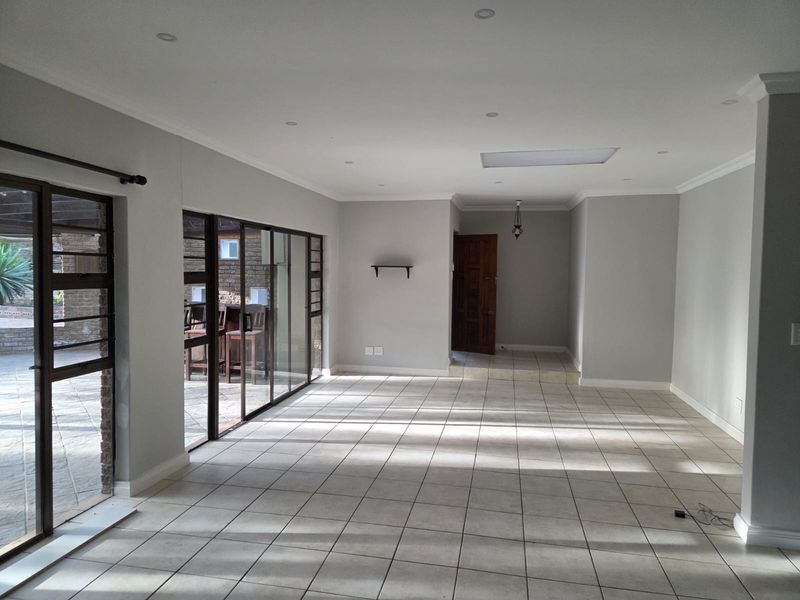 Spacious, light-filled living area featuring neutral tiled flooring, recessed downlights, a skylight, and large sliding glass doors providing seamless access to the outdoor patio.