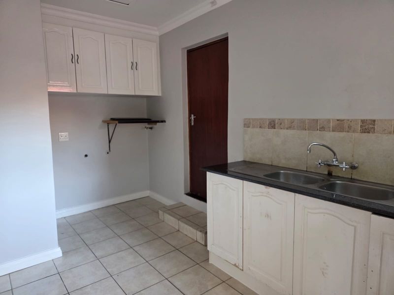 A functional kitchen area featuring built-in white cabinetry, a double bowl sink, tiled splashback, and tiled flooring.