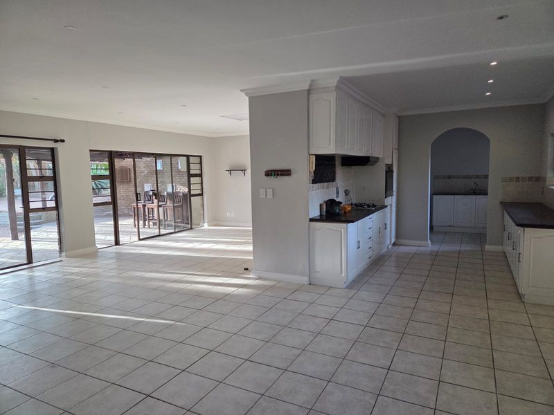 Spacious open-plan living and kitchen area featuring tiled floors, modern white cabinetry, built-in appliances, and large sliding doors leading to an outdoor patio.