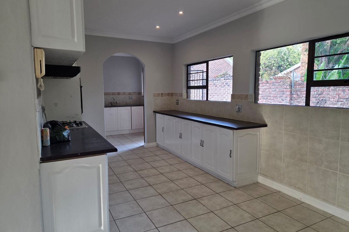 Spacious kitchen featuring white built-in cabinetry, dark laminate countertops, gas hob, extractor fan, and tiled flooring, with an adjoining scullery area.
