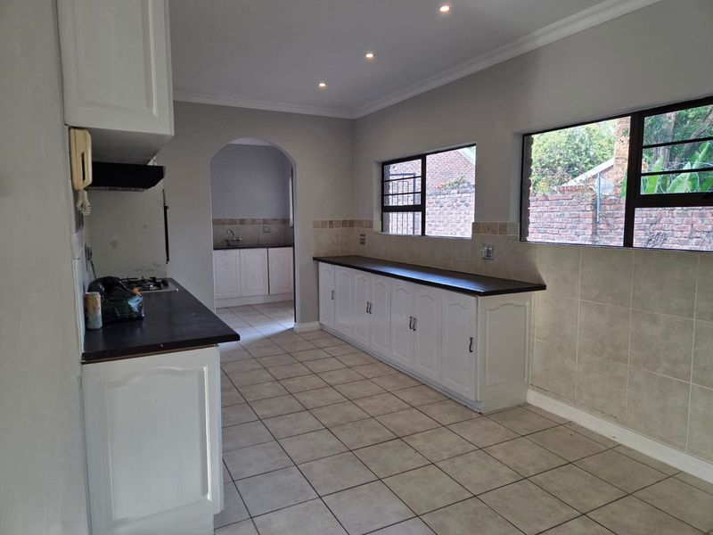 Spacious kitchen featuring white built-in cabinetry, dark laminate countertops, gas hob, extractor fan, and tiled flooring, with an adjoining scullery area.