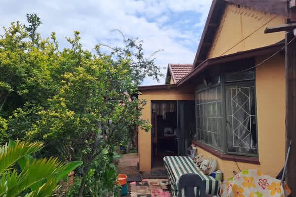 Rear exterior view of the house showing the garden area, tiled roof, and window security bars.