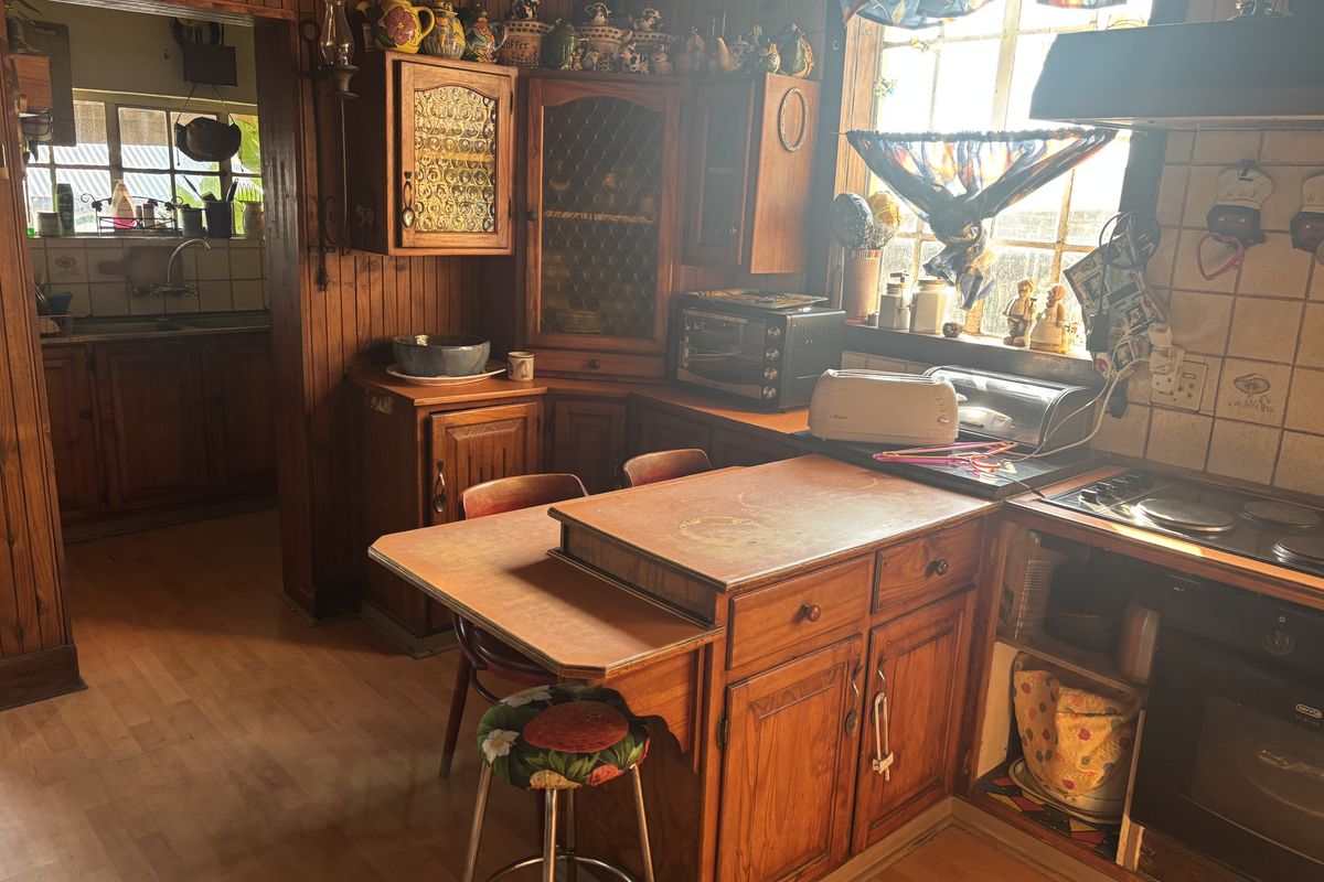 A dated kitchen featuring extensive wooden cabinetry, built-in oven, electric hob, and tiled backsplash, with an adjacent scullery area visible.