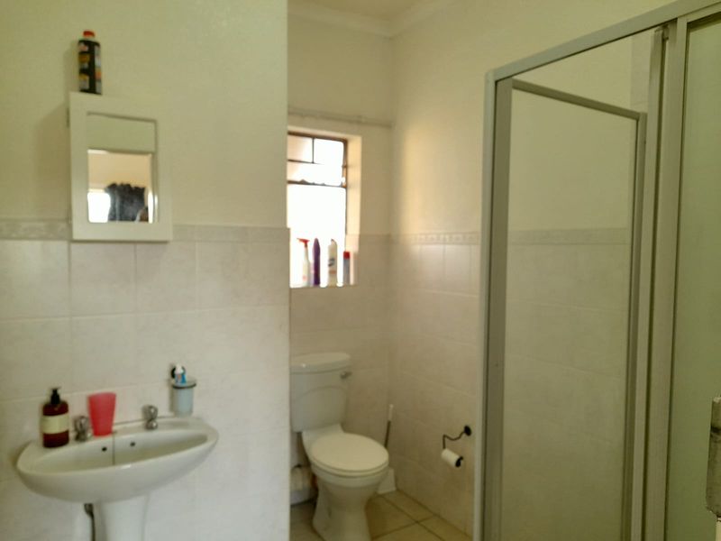 A functional bathroom featuring a pedestal basin, toilet, and a glass-enclosed shower with neutral wall and floor tiling.