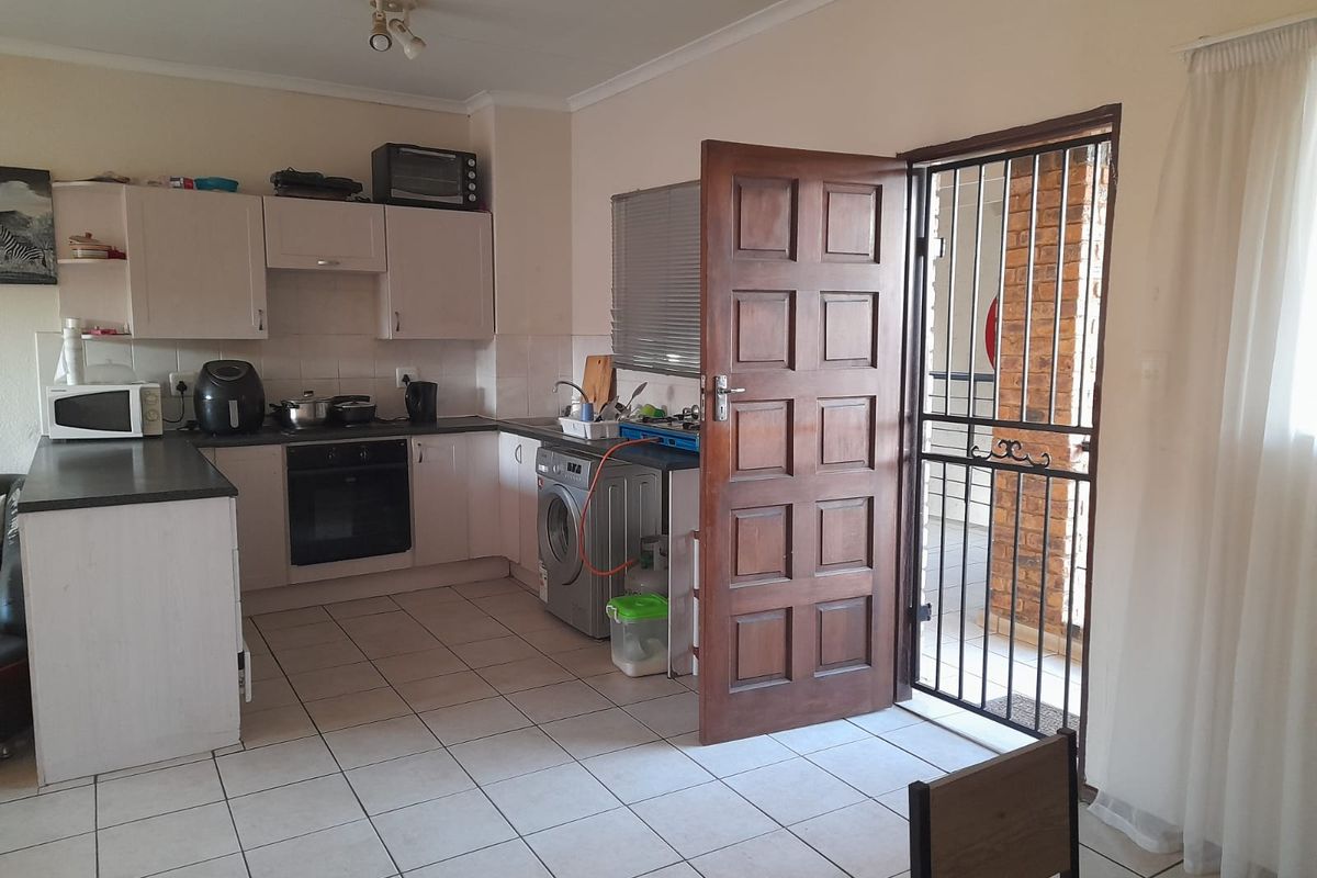 Functional kitchen featuring built-in cabinetry, oven, hob, and tiled flooring, with direct access to an outdoor area through a security gate.