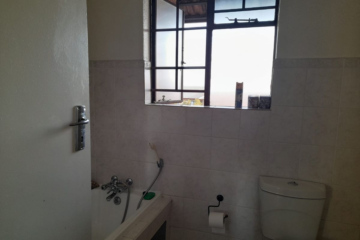 A functional bathroom featuring a bathtub, toilet, and tiled walls, with a window providing natural light. The space is ready for a modern update.