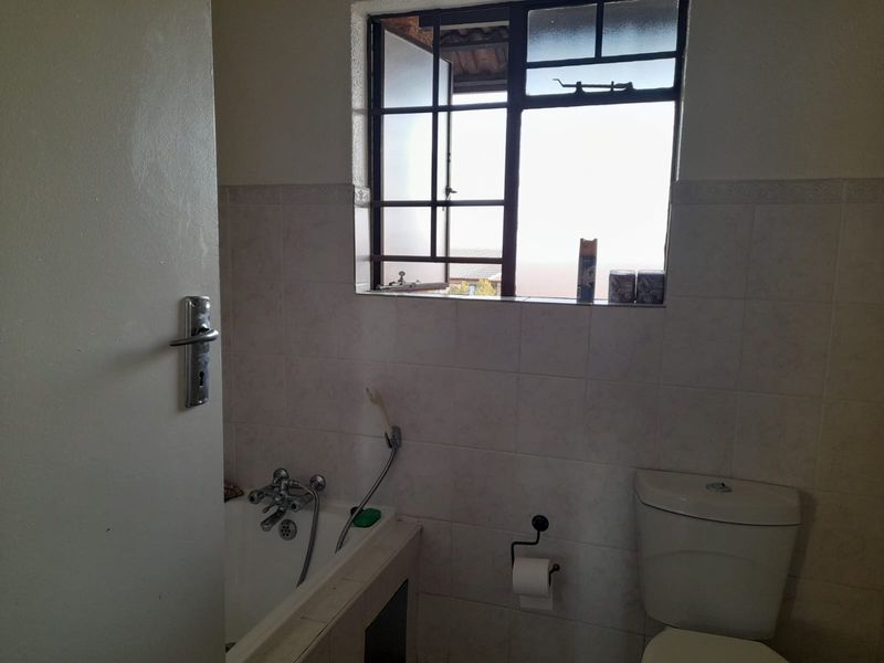 A functional bathroom featuring a bathtub, toilet, and tiled walls, with a window providing natural light. The space is ready for a modern update.