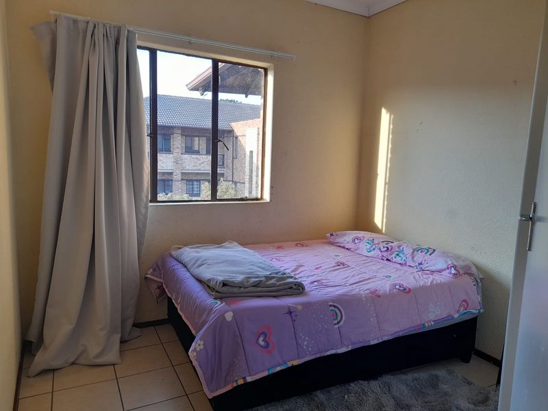 A functional bedroom featuring tiled flooring and a window providing natural light and views of the surrounding apartment complex.