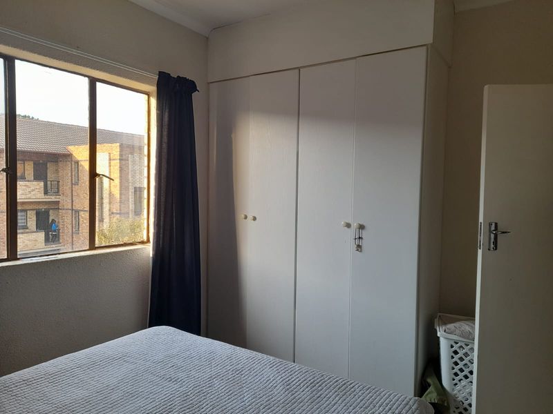 A bedroom featuring a built-in white wardrobe and a window providing natural light and a view of the surrounding apartment complex.