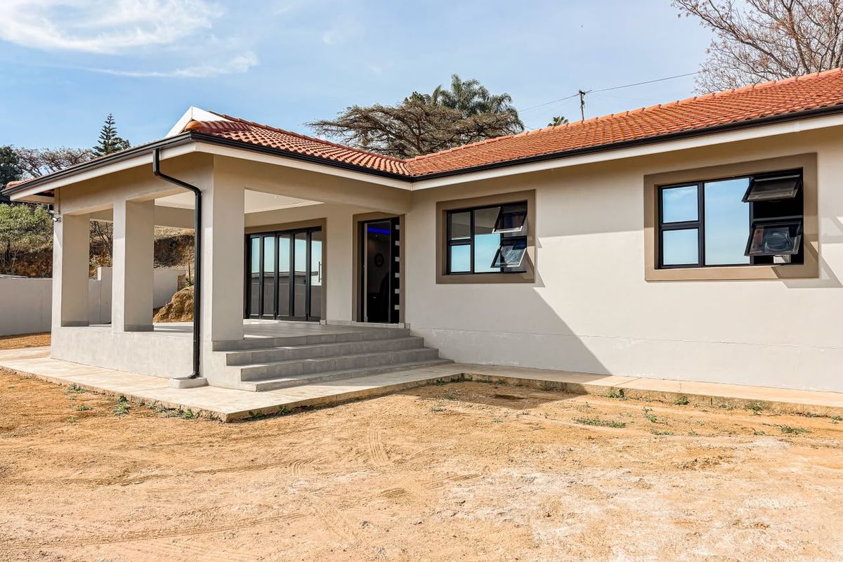 Rear view of a modern house featuring a covered patio, terracotta tiled roof, and aluminium framed windows, set against an unlandscaped garden area.
