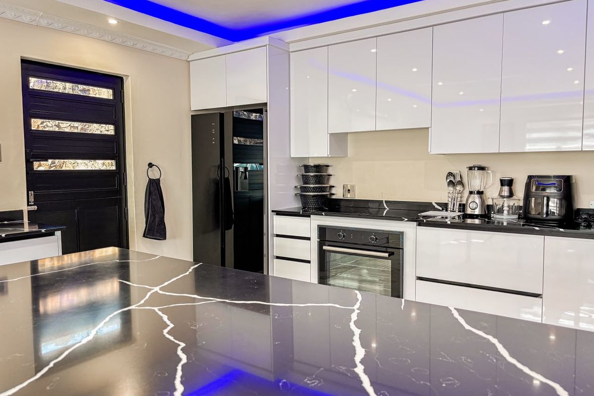 Modern kitchen featuring high-gloss cabinetry, a large stone-topped island, built-in oven, and integrated blue LED cove lighting.