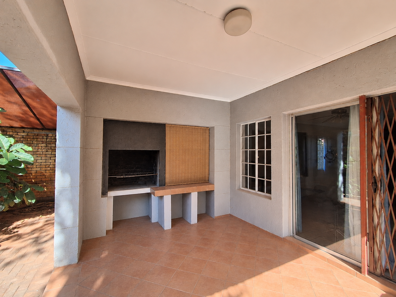 Covered patio area featuring a built-in braai, tiled flooring, and direct access to the interior through a sliding glass door.