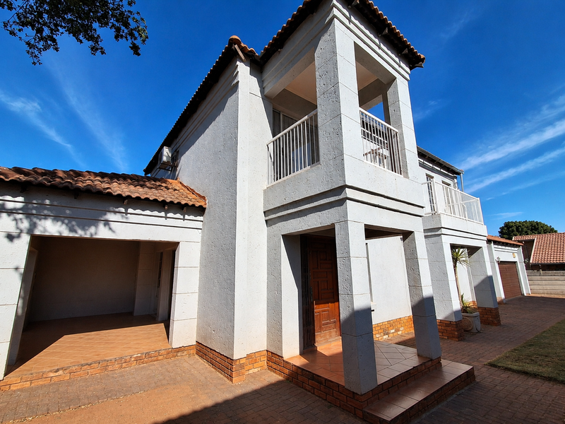 Front elevation of a double-story residence featuring a tiled roof, covered entrance, balcony with metal railings, and paved driveway area.